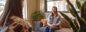 a focused teenager sits in a modern therapy office, surrounded by calming decor, as a therapist engages them in a supportive conversation, embodying the essence of adolescent therapy for managing stress and anger.