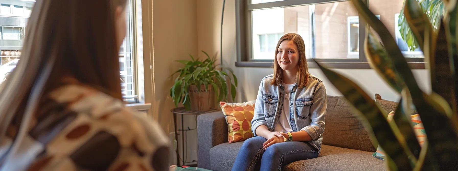 a focused teenager sits in a modern therapy office, surrounded by calming decor, as a therapist engages them in a supportive conversation, embodying the essence of adolescent therapy for managing stress and anger.